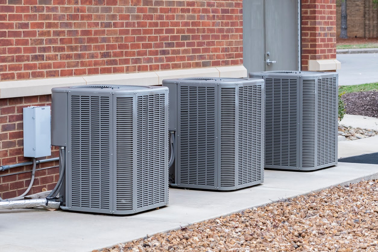 Horizontal shot of commercial air conditioners outside near a maintenance door.